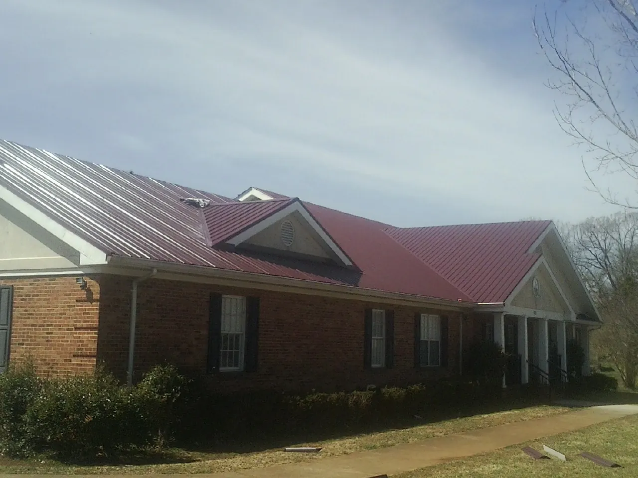 Red metal roof with gabled entries on a long brick building, from a Hail Damage Roof Repair job in Randle