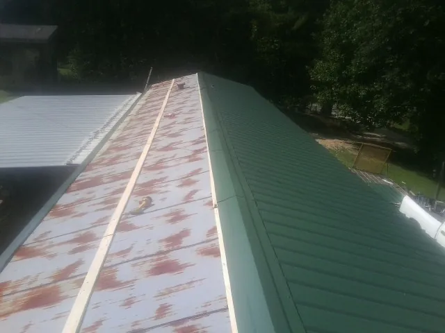 Old rusted panels beside newly installed green metal roofing — Wind Damage Roof Repair by Roofing Brothers in Randle