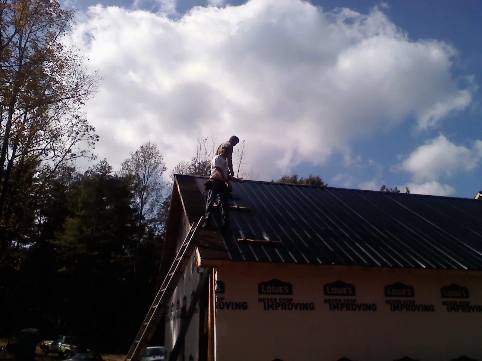 Roofer fastening dark metal panels high against a cloudy sky, from a Roof Inspection job in Randle
