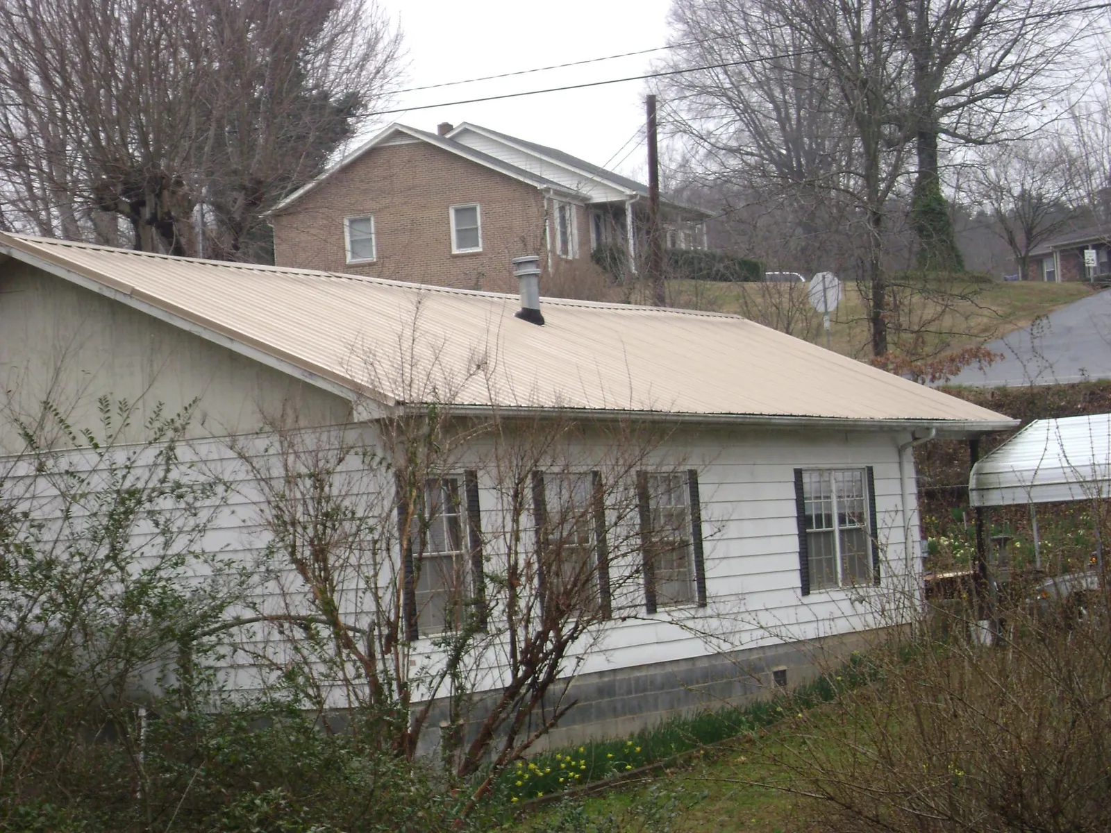 Tan metal roof on a white sided house set into a hillside — Commercial Roofing by Roofing Brothers in Randle