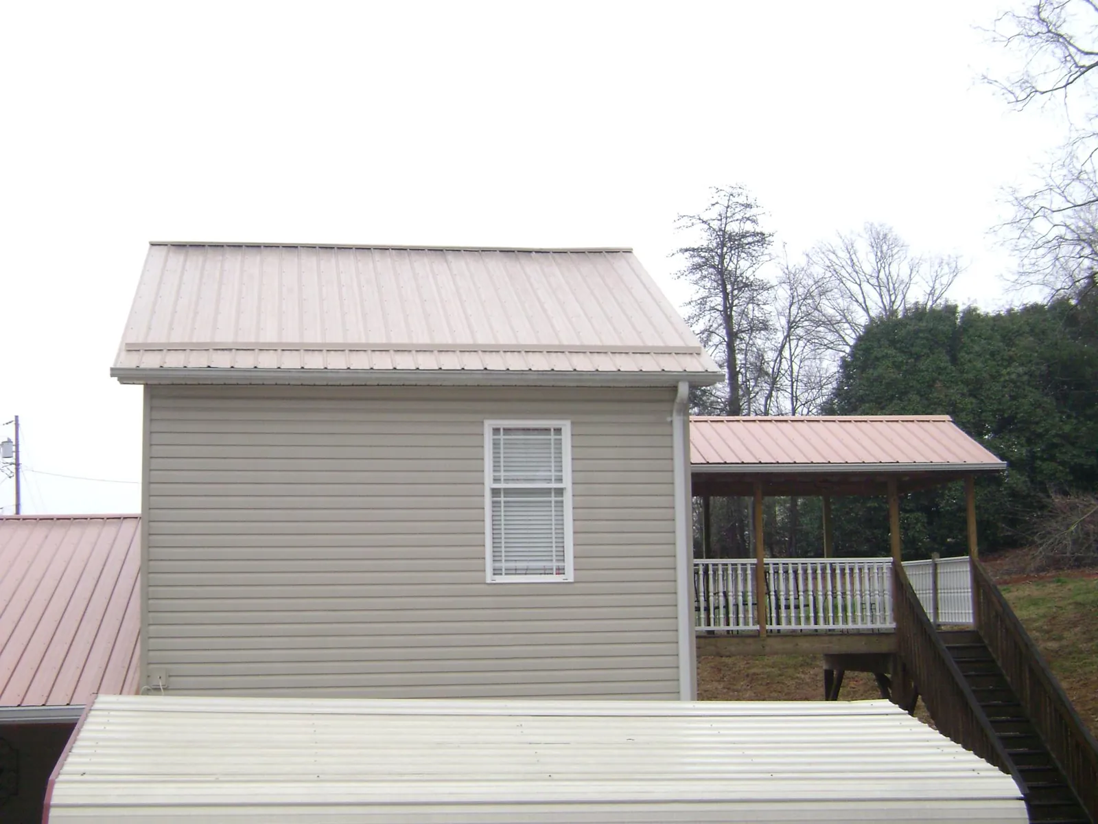 Tan metal roofs on a two story addition and attached porch, from a Roof Replacement job in Randle